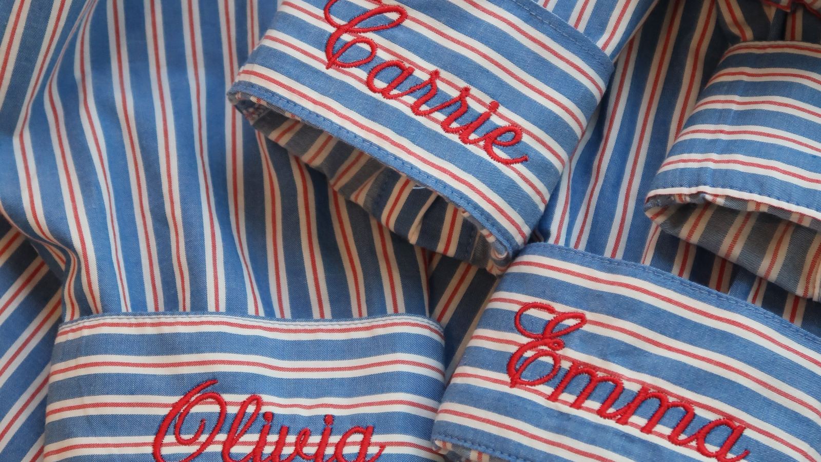 Striped bridesmaid button-down cuffs embroidered with the names Carrie, Olivia and Emma in red script